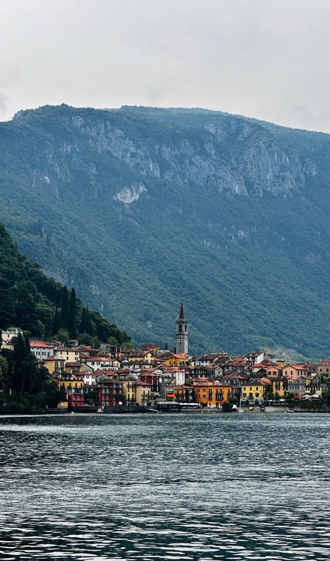 Lakeside village below a steep wooded mountain under grey cloud
